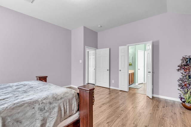 bedroom featuring light hardwood / wood-style floors, lofted ceiling, and connected bathroom