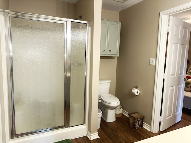 bathroom featuring wood-type flooring, a shower with shower door, and toilet