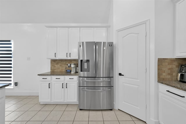 kitchen with white cabinets, stainless steel fridge, dark stone counters, and tasteful backsplash