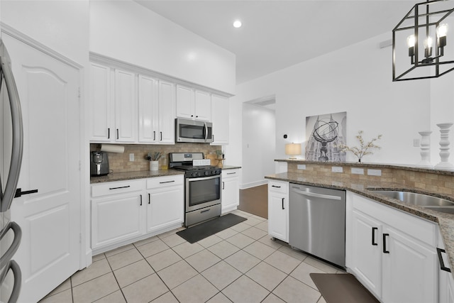 kitchen featuring white cabinetry, backsplash, dark stone counters, decorative light fixtures, and appliances with stainless steel finishes