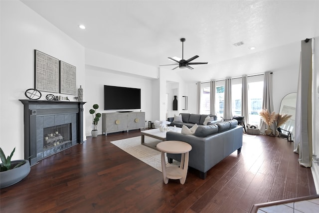 living room with a tile fireplace, vaulted ceiling, ceiling fan, and dark wood-type flooring