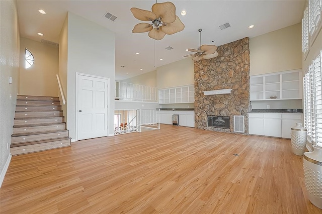 unfurnished living room featuring ceiling fan, light hardwood / wood-style floors, a fireplace, and a high ceiling