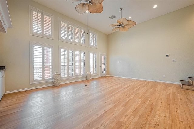 interior space with ceiling fan, light wood-type flooring, and a towering ceiling