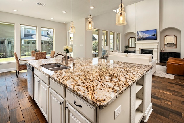 kitchen with a center island with sink, decorative light fixtures, sink, and dark wood-type flooring