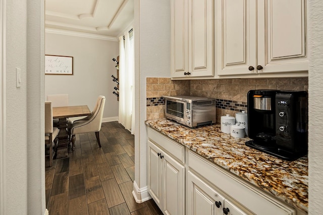 kitchen with decorative backsplash, light stone countertops, dark hardwood / wood-style flooring, and ornamental molding