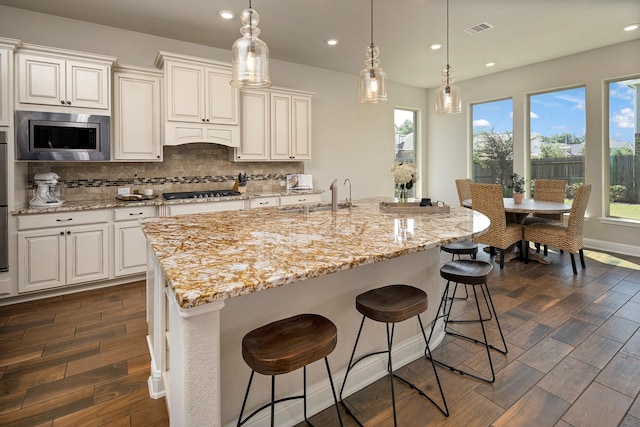 kitchen featuring dark hardwood / wood-style floors, an island with sink, tasteful backsplash, white cabinetry, and stainless steel appliances