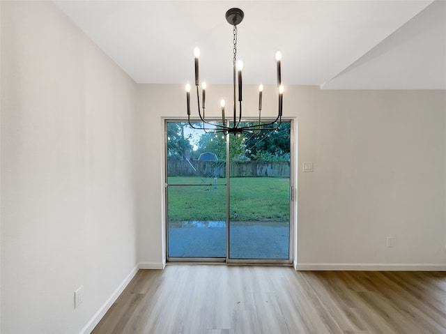 unfurnished dining area with wood-type flooring and a chandelier