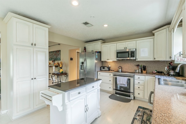 kitchen featuring white cabinetry, sink, backsplash, appliances with stainless steel finishes, and light wood-type flooring