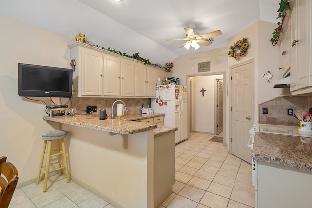 kitchen featuring a breakfast bar, tasteful backsplash, white refrigerator with ice dispenser, and vaulted ceiling