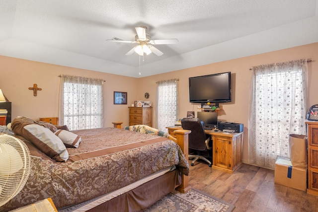 bedroom with a tray ceiling, ceiling fan, hardwood / wood-style floors, and a textured ceiling