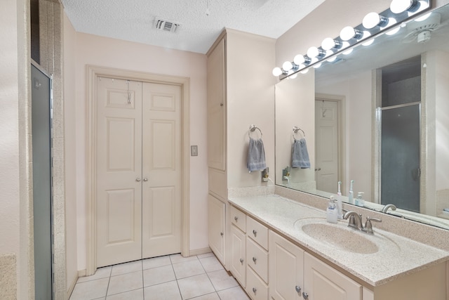 bathroom featuring tile patterned flooring, vanity, a shower with shower door, and a textured ceiling