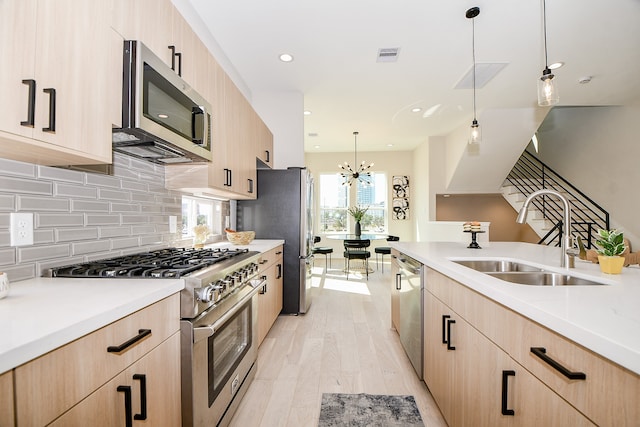 kitchen featuring appliances with stainless steel finishes, sink, light brown cabinets, decorative light fixtures, and light hardwood / wood-style flooring