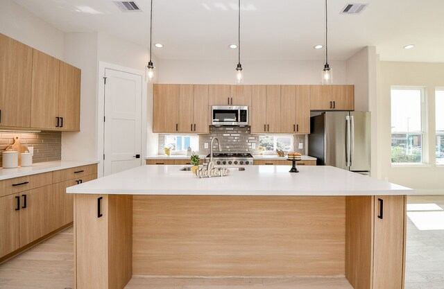 kitchen featuring light brown cabinets, stainless steel appliances, light hardwood / wood-style flooring, and an island with sink