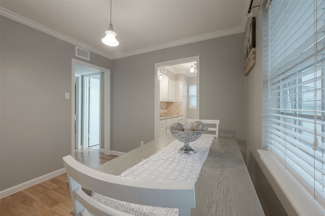 dining space featuring sink, light wood-type flooring, and crown molding