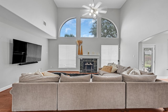 living room with ceiling fan, wood-type flooring, a fireplace, and a high ceiling