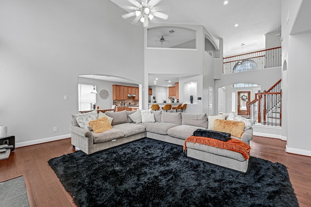 living room with a high ceiling, ceiling fan, and dark wood-type flooring