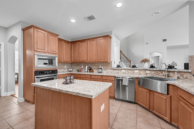 kitchen with light stone countertops, stainless steel appliances, sink, a kitchen island, and lofted ceiling