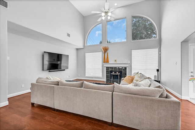 living room with ceiling fan, a fireplace, dark wood-type flooring, and a high ceiling