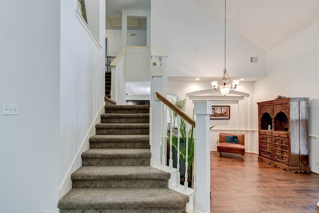 staircase with hardwood / wood-style floors, high vaulted ceiling, and an inviting chandelier