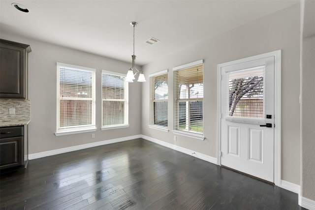 unfurnished dining area with dark wood-type flooring and an inviting chandelier