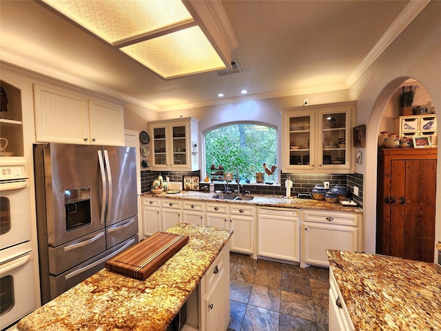 kitchen featuring arched walkways, white appliances, tasteful backsplash, and a sink