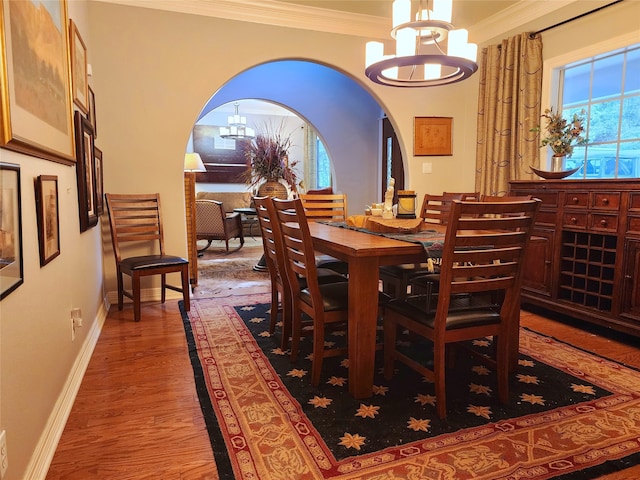 dining room with baseboards, ornamental molding, an inviting chandelier, wood finished floors, and arched walkways