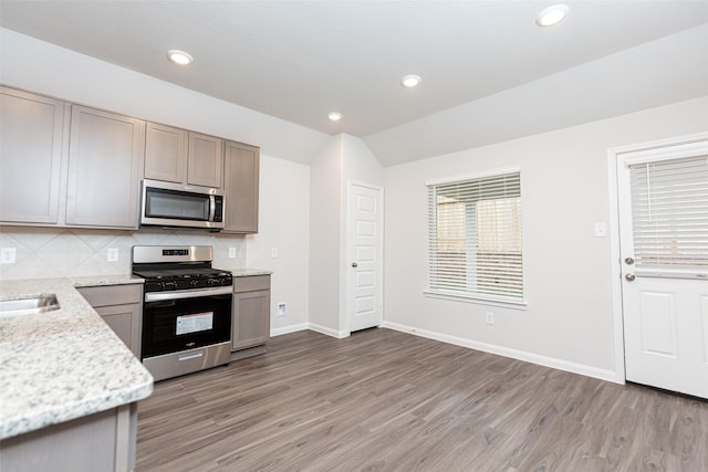 kitchen featuring decorative backsplash, light stone counters, stainless steel appliances, wood-type flooring, and lofted ceiling