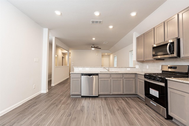 kitchen with light stone countertops, kitchen peninsula, stainless steel appliances, ceiling fan, and light hardwood / wood-style flooring