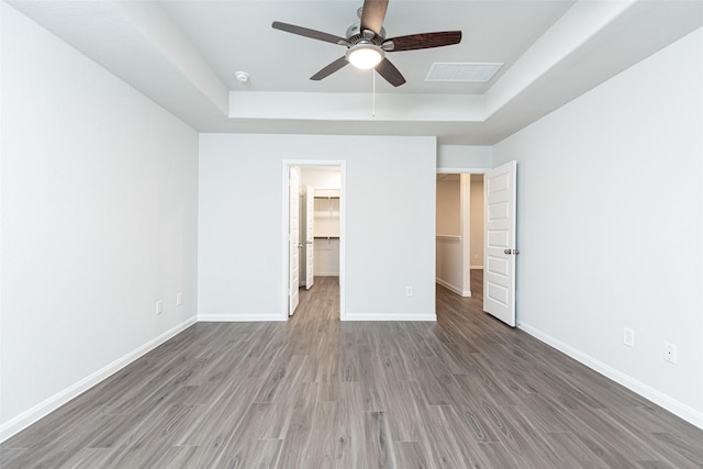 unfurnished bedroom with a walk in closet, a raised ceiling, ceiling fan, hardwood / wood-style floors, and a closet