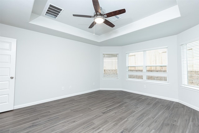 empty room with plenty of natural light, dark hardwood / wood-style floors, and a raised ceiling