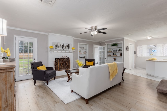 living room with built in shelves, ceiling fan, light hardwood / wood-style floors, a textured ceiling, and ornamental molding