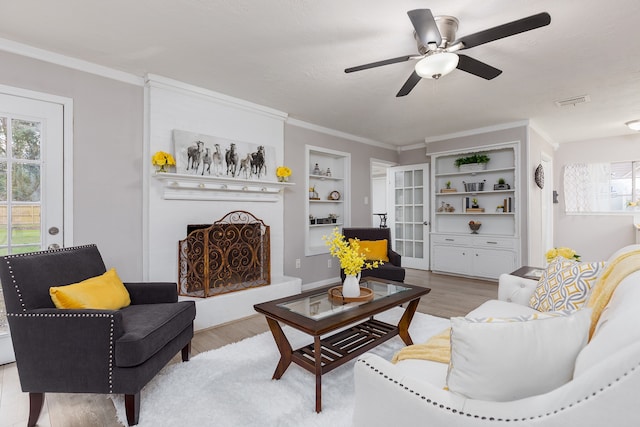 living room with ceiling fan, built in shelves, ornamental molding, a textured ceiling, and light hardwood / wood-style floors