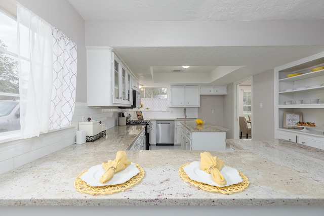 kitchen with light stone countertops, appliances with stainless steel finishes, backsplash, and white cabinetry