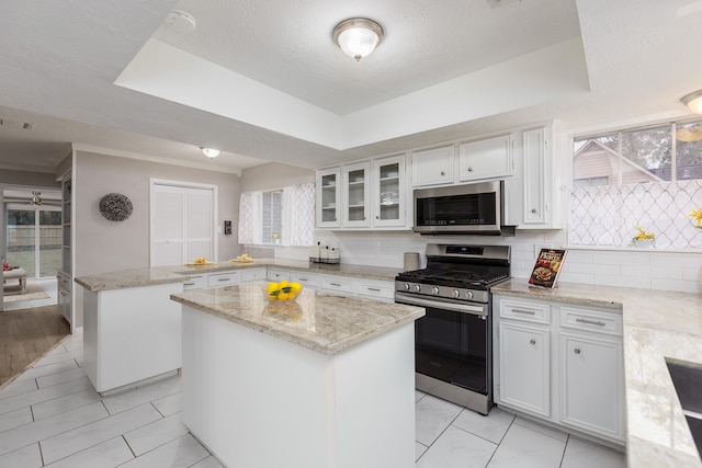 kitchen featuring a center island, backsplash, white cabinets, light stone counters, and stainless steel appliances