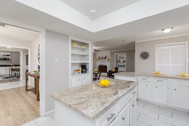 kitchen featuring built in shelves, light stone countertops, white cabinetry, light hardwood / wood-style floors, and a kitchen island