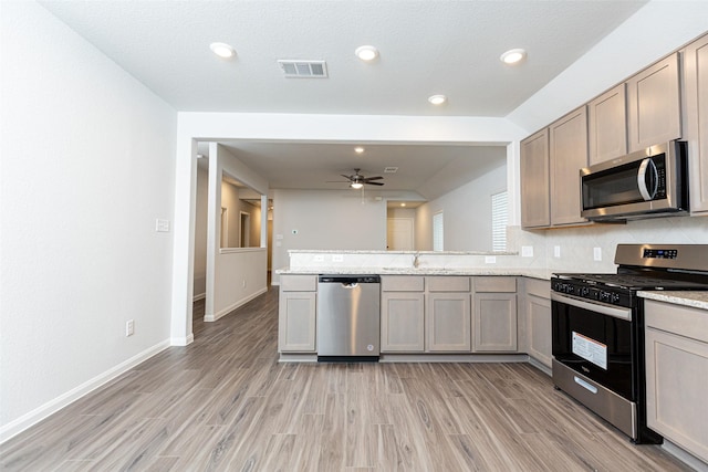 kitchen featuring kitchen peninsula, appliances with stainless steel finishes, light stone counters, ceiling fan, and light hardwood / wood-style flooring