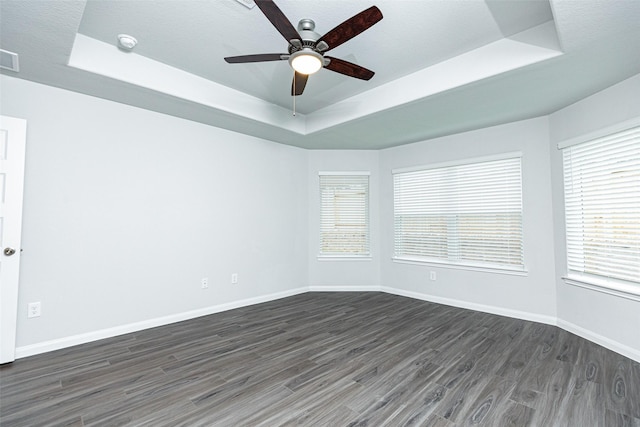 empty room featuring dark hardwood / wood-style floors, ceiling fan, and a raised ceiling