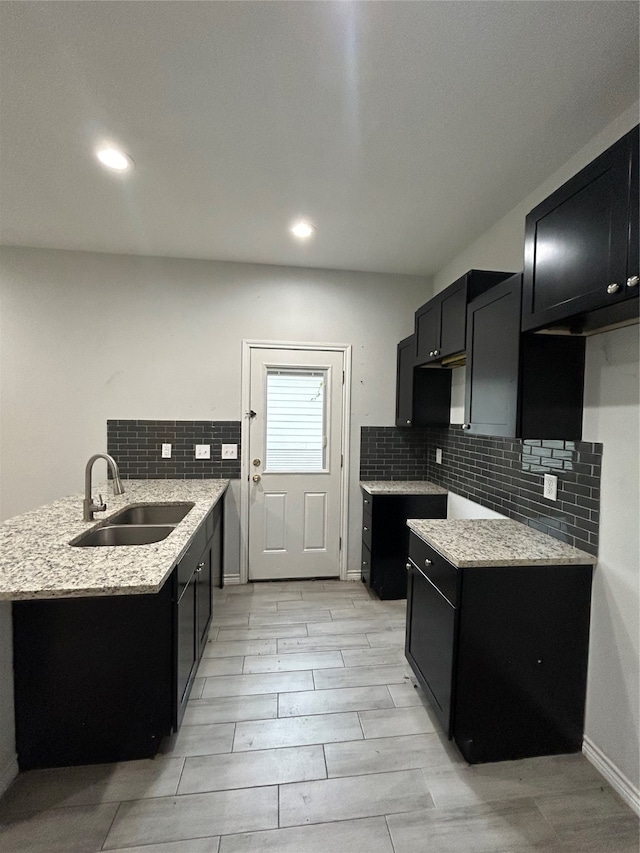 kitchen with light stone countertops, backsplash, light hardwood / wood-style floors, and sink