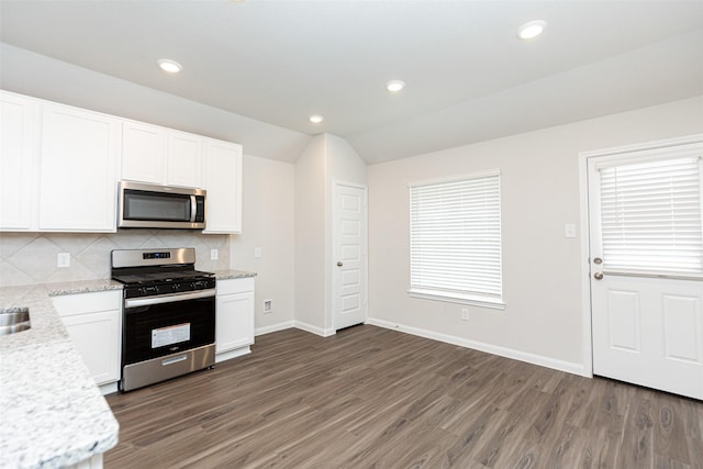 kitchen with appliances with stainless steel finishes, backsplash, vaulted ceiling, dark hardwood / wood-style floors, and white cabinetry