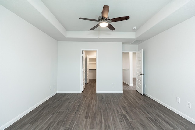 unfurnished bedroom featuring a walk in closet, a raised ceiling, ceiling fan, dark hardwood / wood-style floors, and a closet