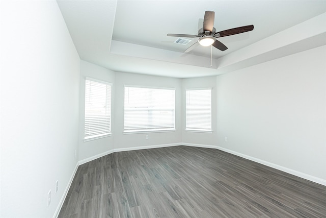 empty room with a raised ceiling, ceiling fan, and dark hardwood / wood-style flooring