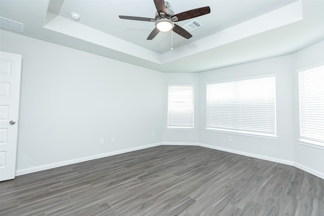 empty room with dark hardwood / wood-style floors, ceiling fan, and a raised ceiling