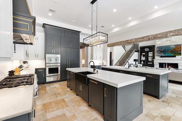 kitchen with sink, hanging light fixtures, a center island with sink, a large fireplace, and appliances with stainless steel finishes