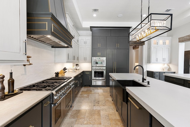 kitchen with decorative light fixtures, white cabinetry, sink, stainless steel appliances, and custom range hood