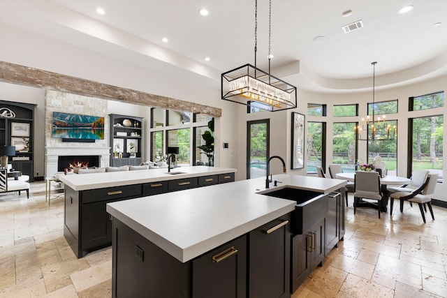 kitchen with sink, a kitchen island with sink, a tray ceiling, a fireplace, and decorative light fixtures