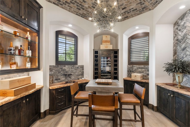 bar with lofted ceiling, brick ceiling, dark brown cabinetry, light stone countertops, and light hardwood / wood-style floors