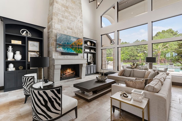 living room featuring a towering ceiling, a stone fireplace, and built in features