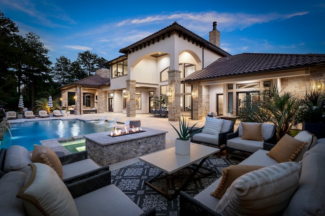 back house at dusk featuring a balcony, pool water feature, an outdoor living space with a fire pit, and a patio area