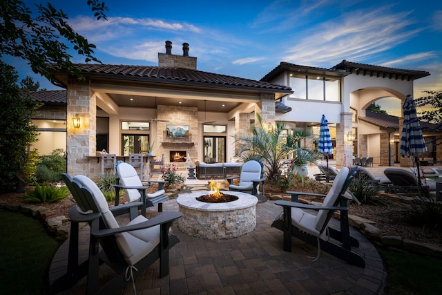 patio terrace at dusk with an outdoor fire pit and an outdoor stone fireplace