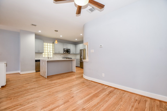 kitchen featuring sink, light wood-type flooring, appliances with stainless steel finishes, decorative light fixtures, and a kitchen island